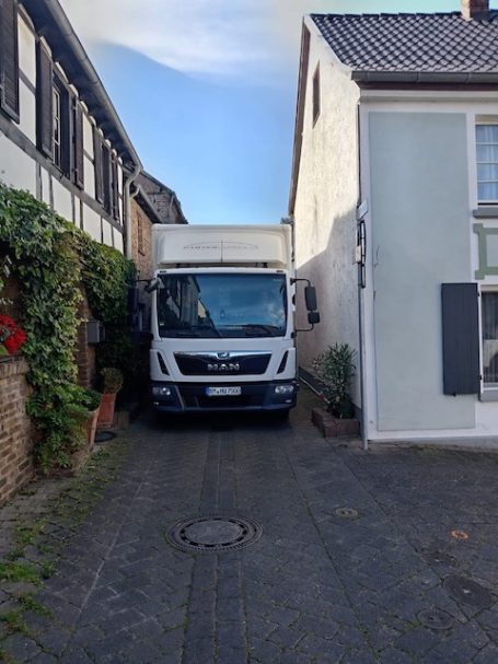 Lieferwagen steht eng zwischen zwei Häusern in einer schmalen Straße.